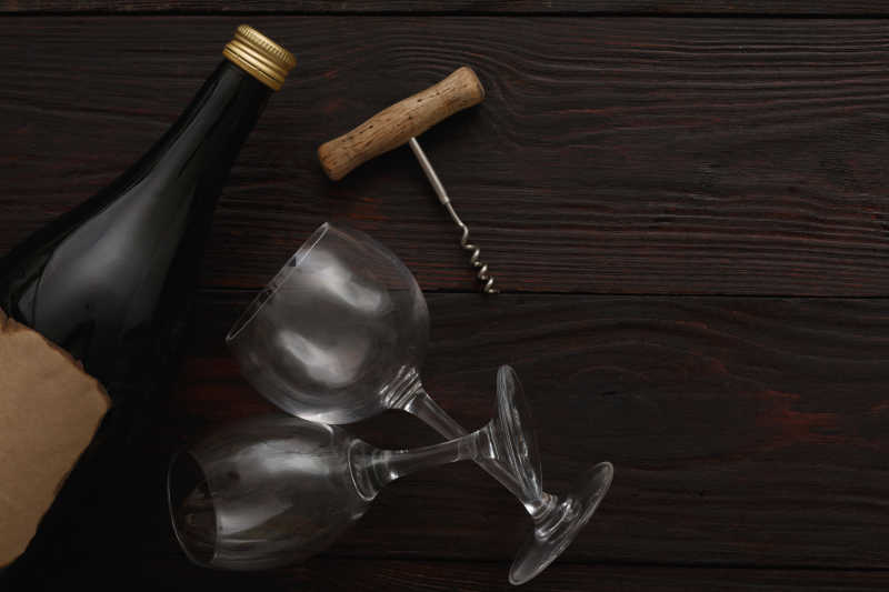 木质桌板上的一瓶红酒一支开瓶器和两只空酒杯