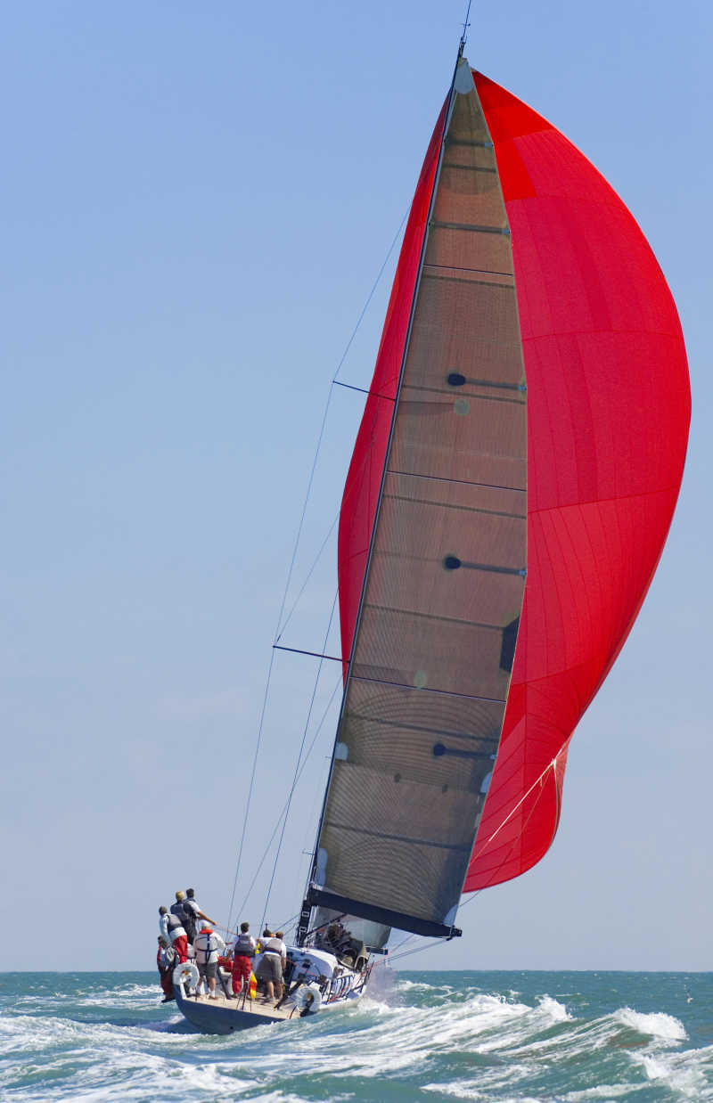 一艘满载人的红色三角帆船在海上航行