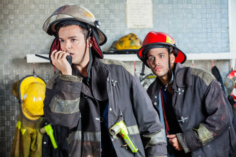 男消防队员在消防站使用对讲机与同事站在一起
