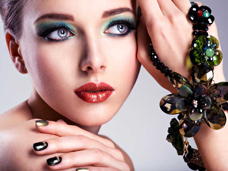 漂亮的女人脸上有时尚绿色化妆品和珠宝