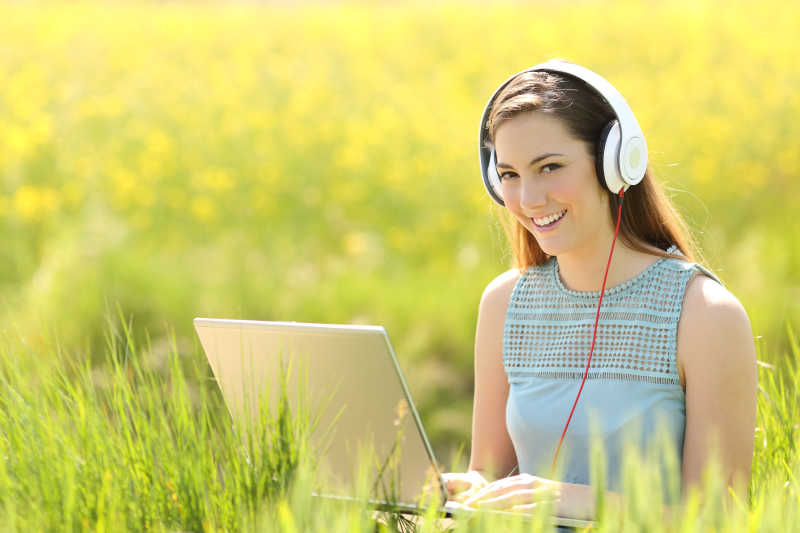 在田野里用笔记本电脑戴耳机听音乐的女人