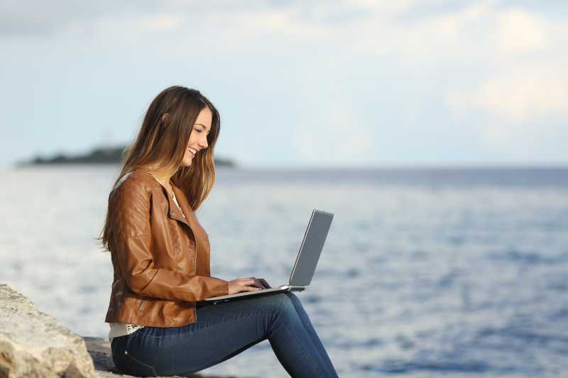 在海滩上用笔记本电脑工作的职业妇女