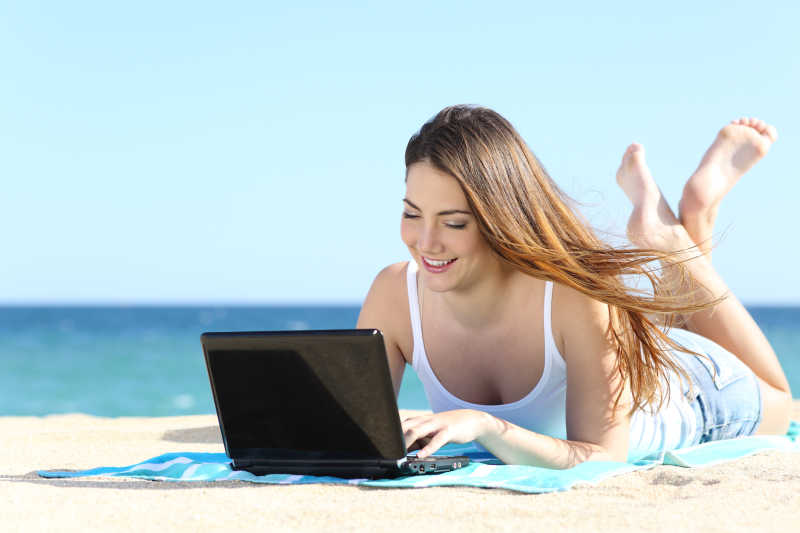 在海滩上使用笔记本电脑学习的快乐女人