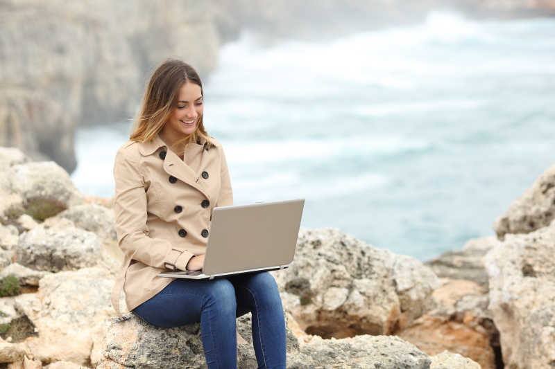 美丽女人在海滩岩石上使用笔记本电脑工作