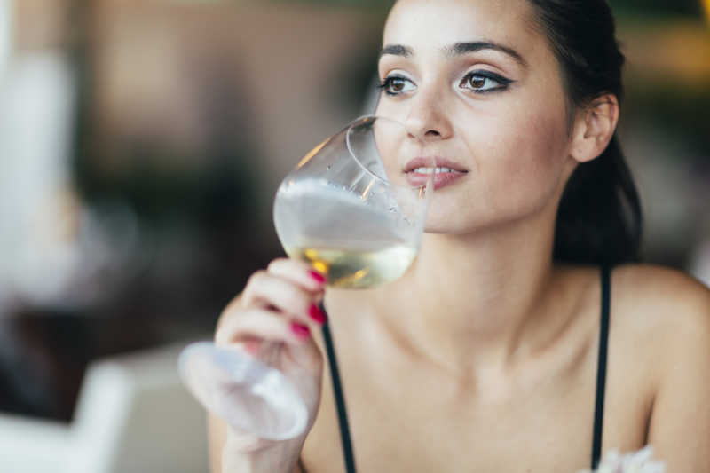 迷人的女人品尝白葡萄酒