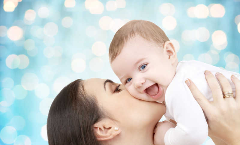 快乐的母亲在蓝色的灯光下亲吻她的婴儿