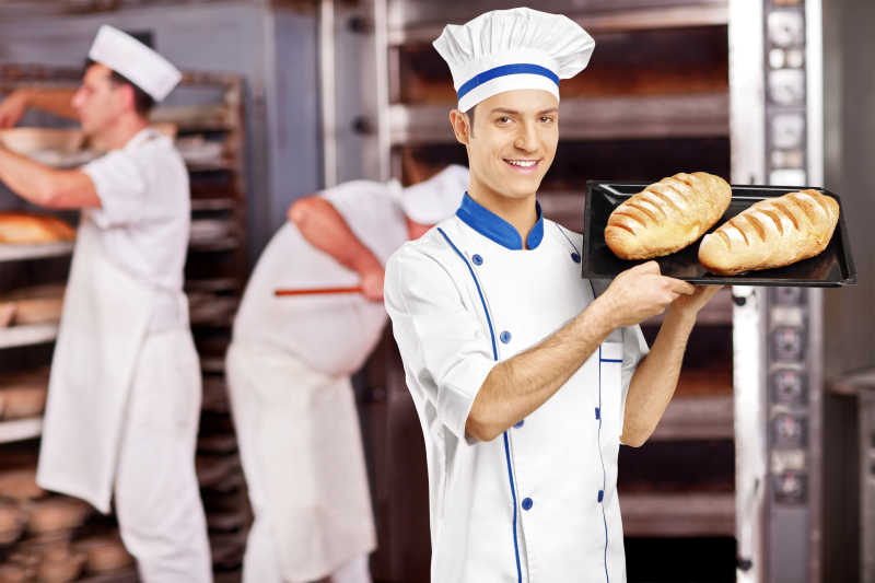 微笑的男面包师在面包店摆上刚出炉的面包