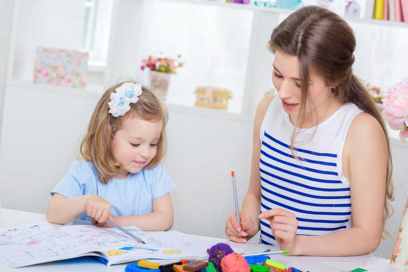 年轻美丽的妈妈和她的小女儿在相册上用铅笔画画