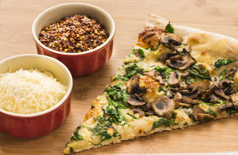 桌上放着的蘑菇菠菜切片披萨和红辣椒片干酪