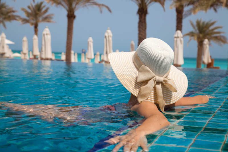 戴大草帽的女人在异国情调的游泳池里放松