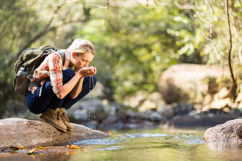 年轻的旅行者在山间饮用溪水