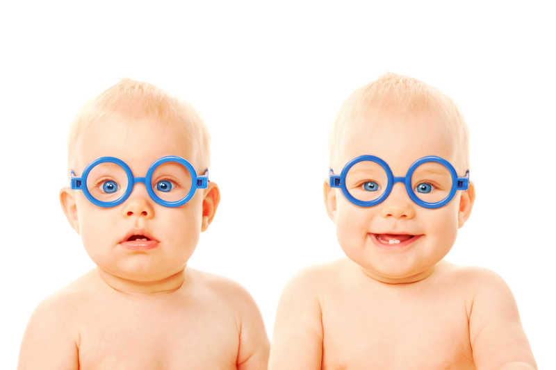 白色背景下带着蓝色眼镜搞怪的双胞胎宝宝