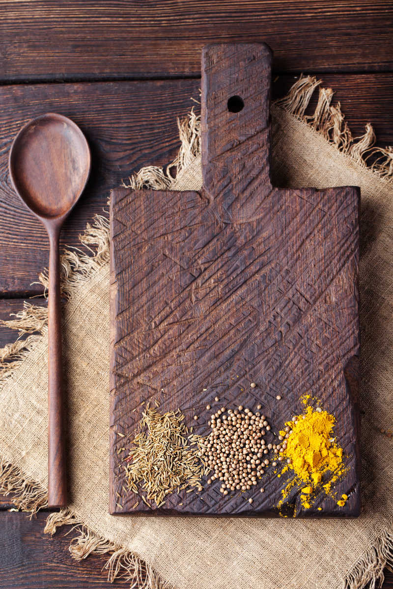 木制砧板孜然姜黄芫荽种子和勺子放在一个旧木桌上