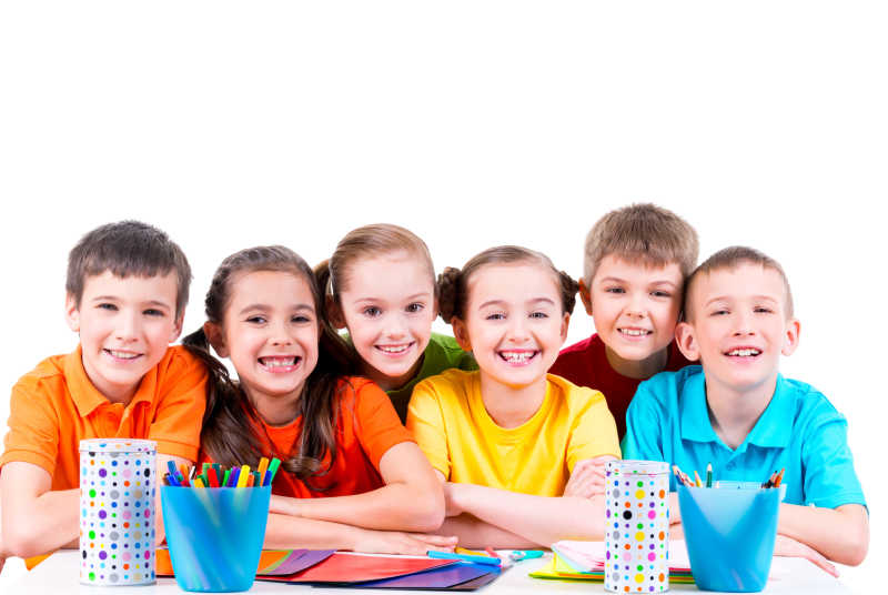 孩子们围坐在彩笔蜡笔和彩色纸板的桌旁对着镜头微笑