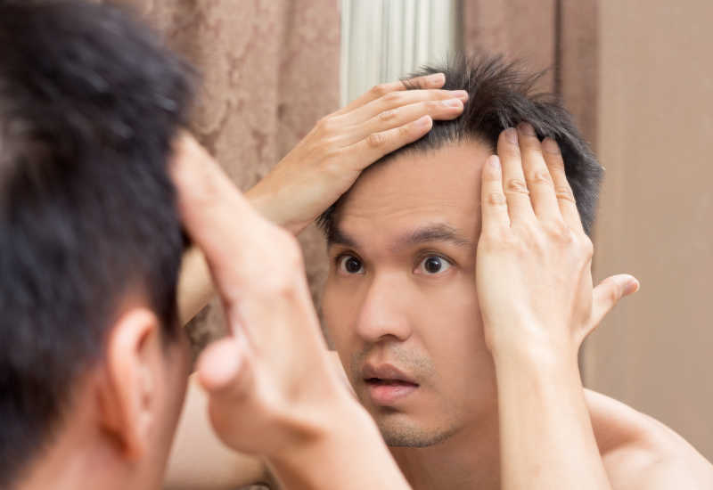 照着镜子看自己的头发的亚洲男性
