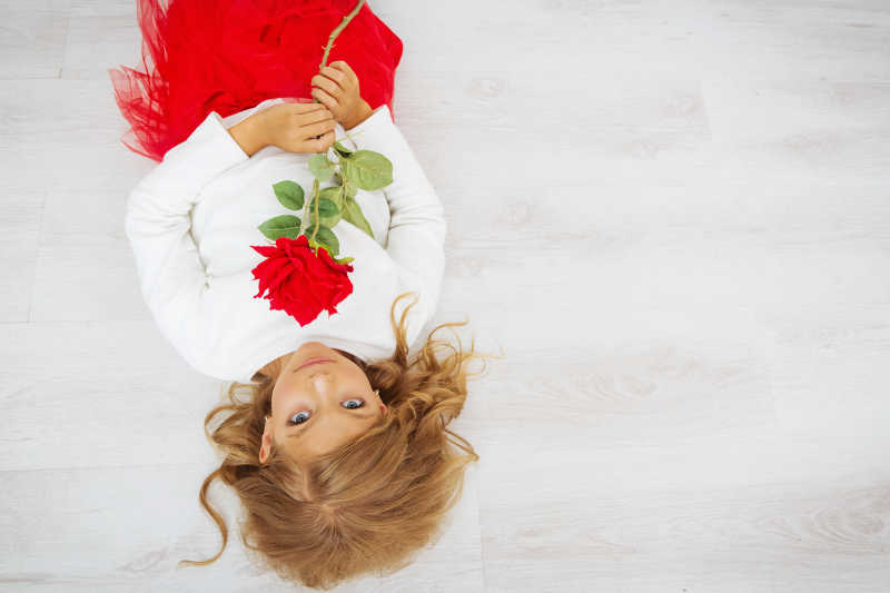 躺在木地板上拿着玫瑰花的小女孩