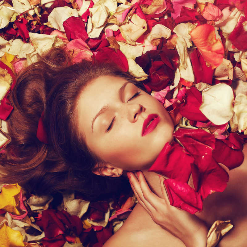 躺在凋谢的玫瑰花瓣上的女模特