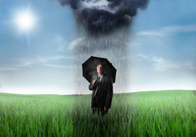 站在草地上拿着黑色雨伞下着概念雨的商人