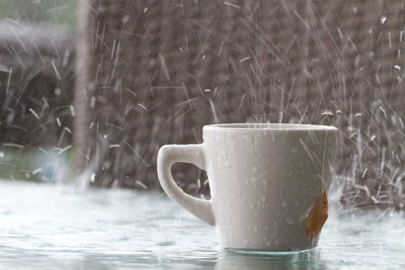 户外雨水滴落在放有白色咖啡杯的玻璃桌面上飞溅特写