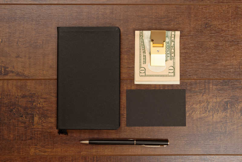 深棕色木板上的笔记本和黑色空白名片