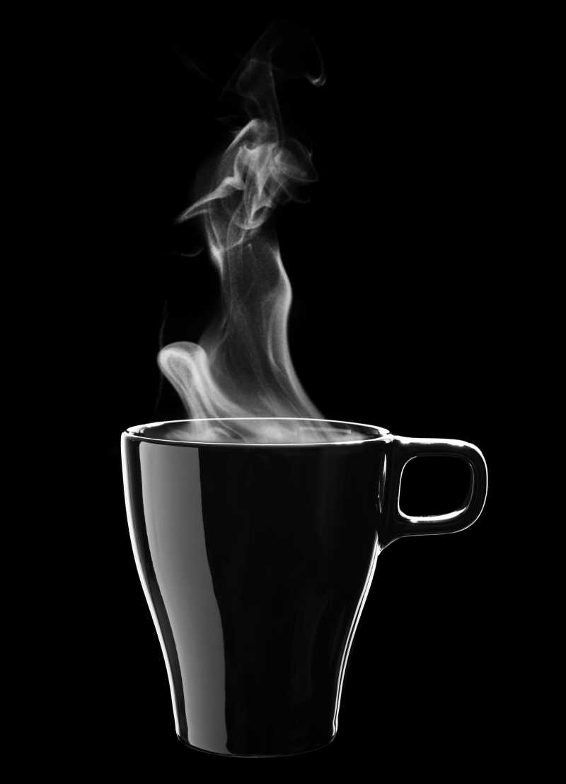 黑色背景下冒着热气的黑色咖啡杯