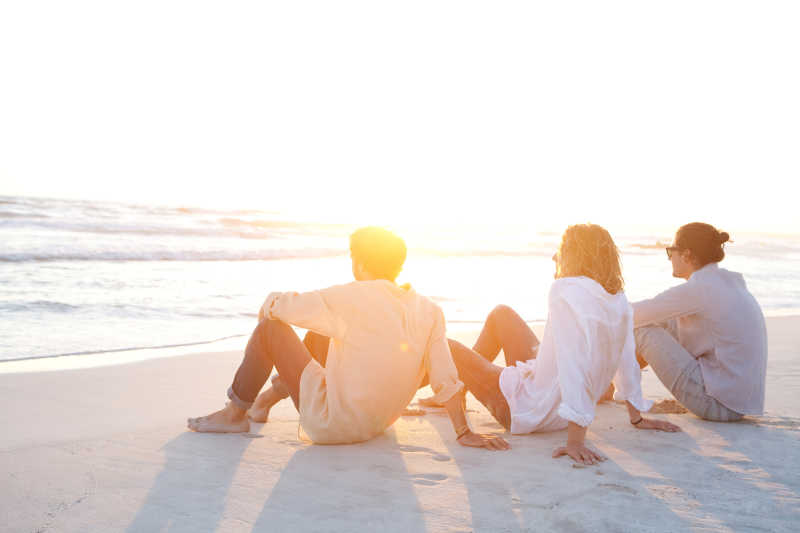 三位朋友坐在一座白沙海滩上