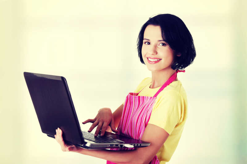 穿粉红色的围裙现代家庭主妇或女职工与笔记本电脑