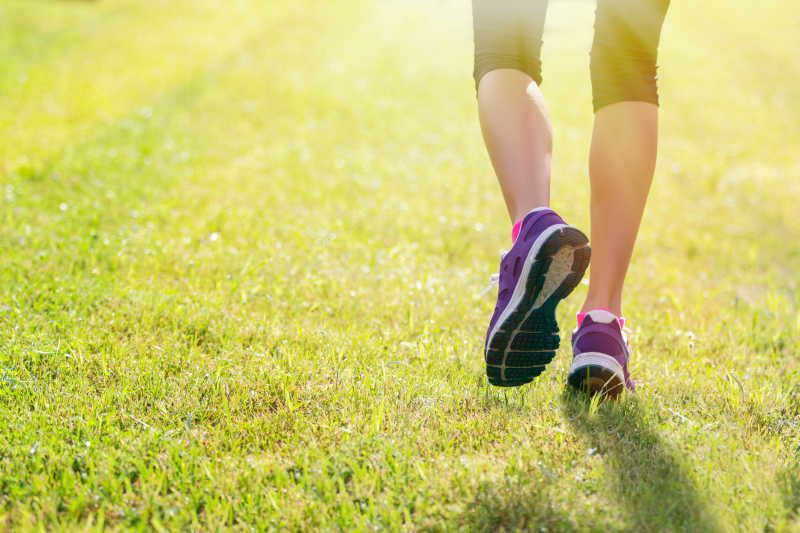 阳光下在草坪上穿着运动鞋跑步的人