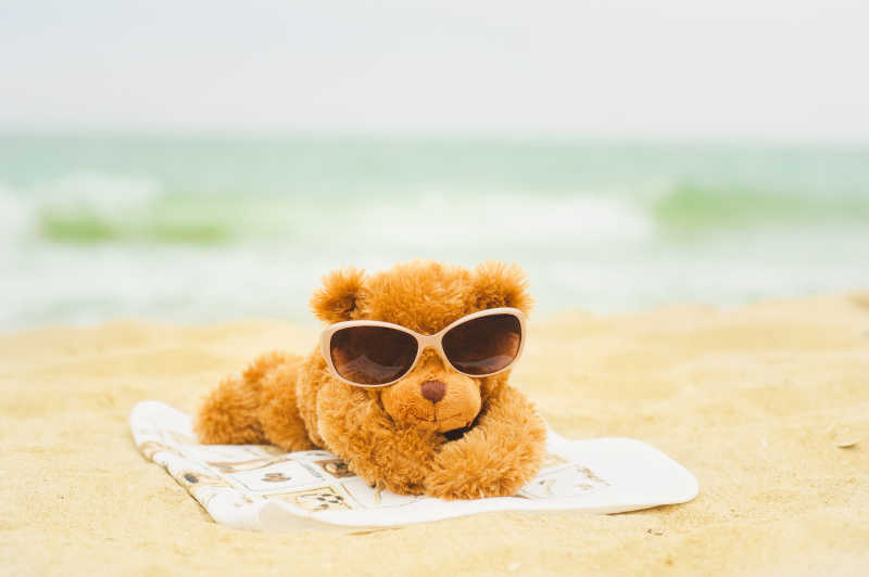 趴在沙滩上戴着墨镜的泰迪熊