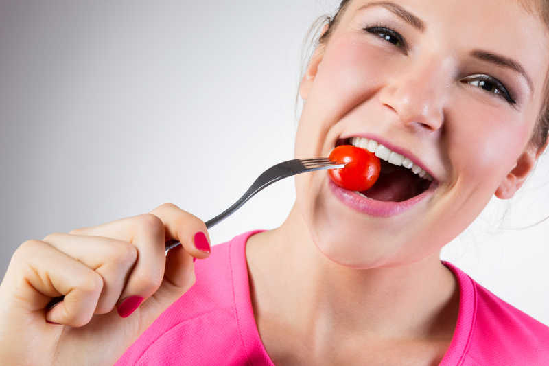 快乐的女人正在吃樱桃番茄