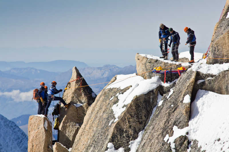 群山背景下在覆盖着白雪的勃朗峰山丘上攀登的高山登山者