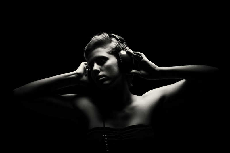 黑色背景下的女人带着耳机听音乐