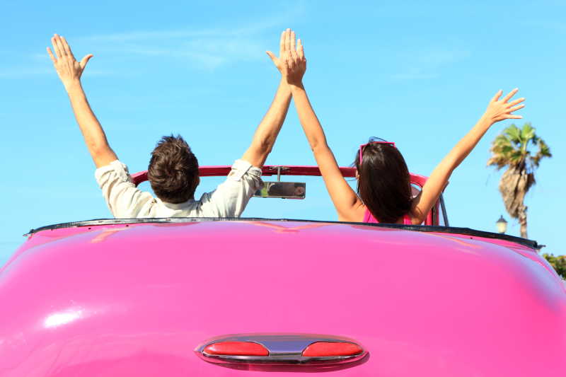 快乐的情侣驾驶粉红色复古汽车欢呼喜悦举起手臂