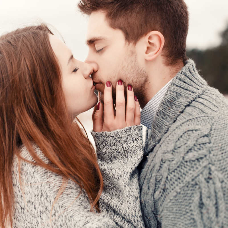 穿着毛衣的年轻情侣在户外接吻