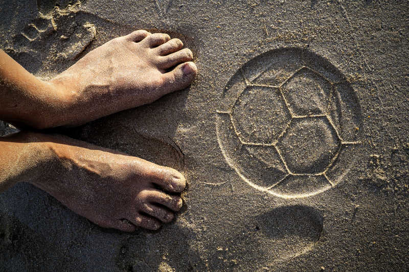 两只脚和沙滩上足球的痕迹