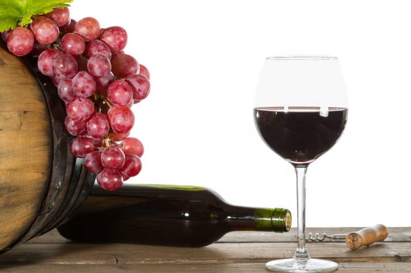 桌子上的红酒杯瓶子和放在木桶上的新鲜葡萄