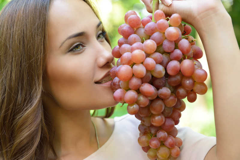 美丽的女人抱着成熟的葡萄束