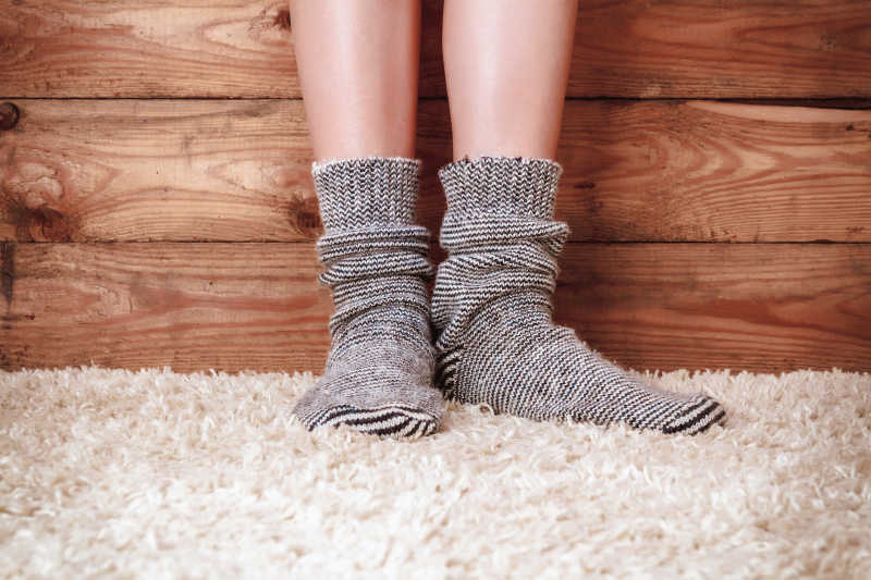 一双穿灰色袜子腿站在地毯上