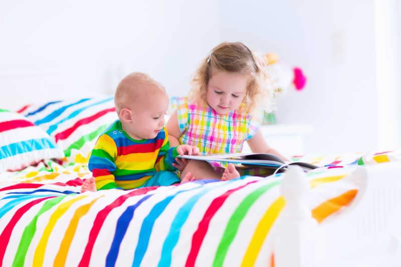 小姐弟俩坐在五颜六色的彩虹床上看书