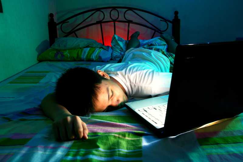 少年在床上睡着身边放着笔记本电脑