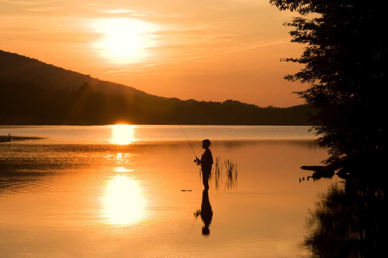 日出时在湖上钓鱼的男孩剪影