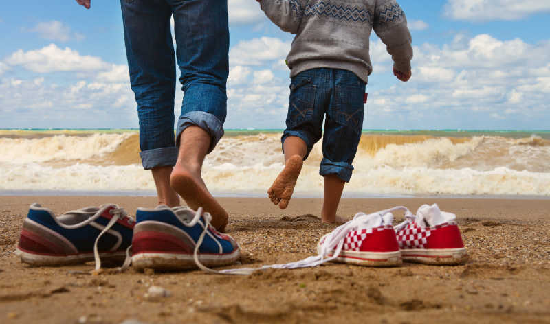 父亲和儿子光脚在海边散步