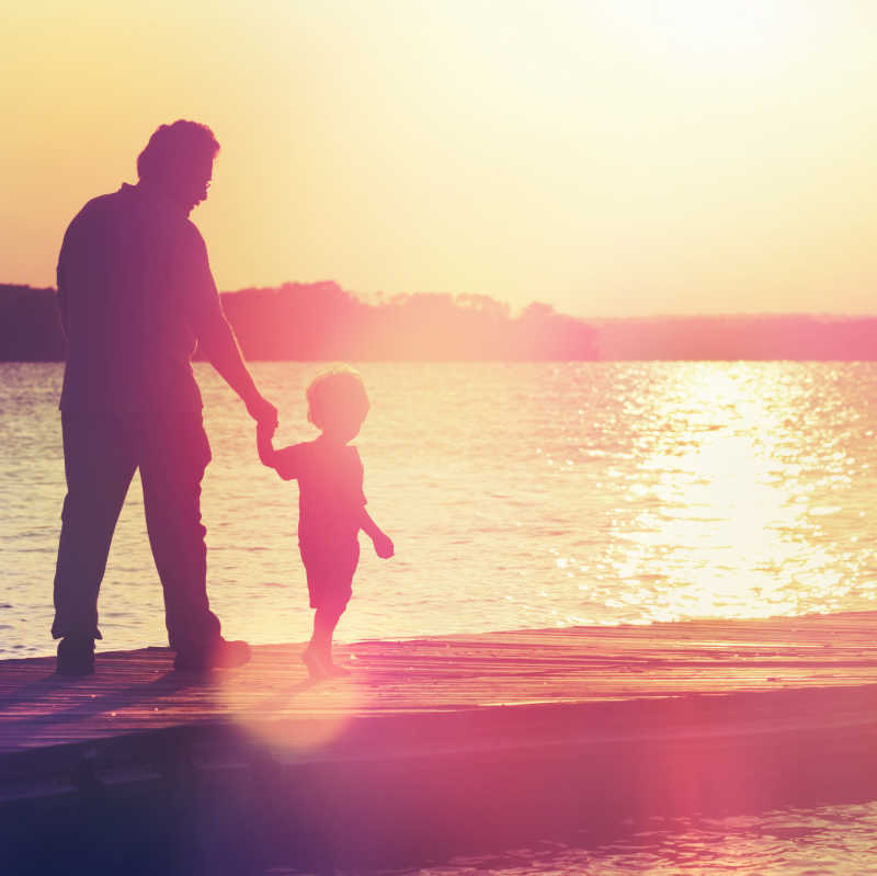 父亲和儿子走在码头日落的阳光下
