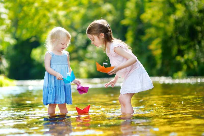 阳光明媚的河流里玩纸船的小女孩