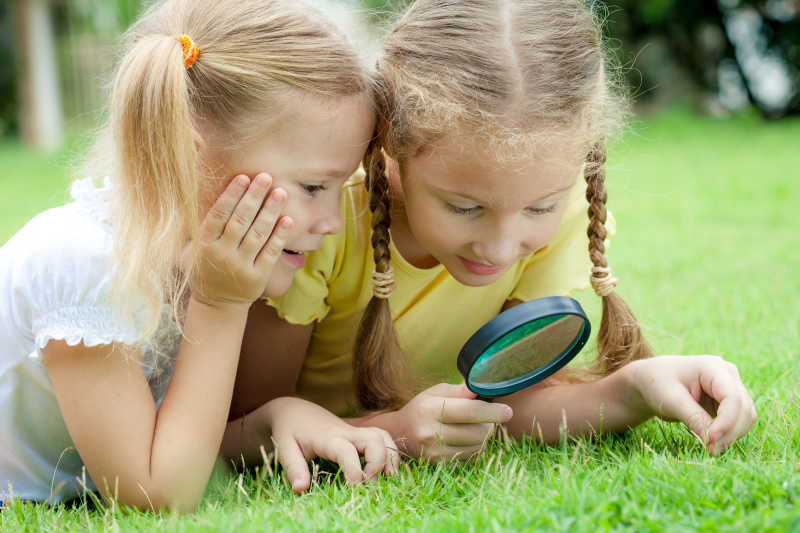 草地上拿着放大镜的两个小女孩