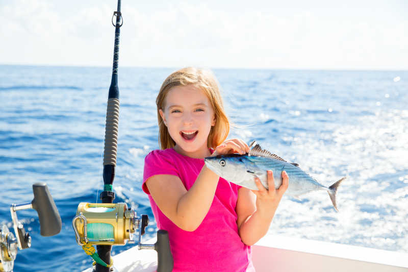 钓鱼的小女孩拿着钓到的金枪鱼兴奋的笑着