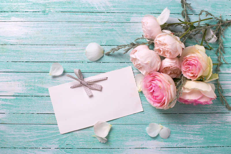 淡蓝色木桌上的明信片与新鲜粉色玫瑰花