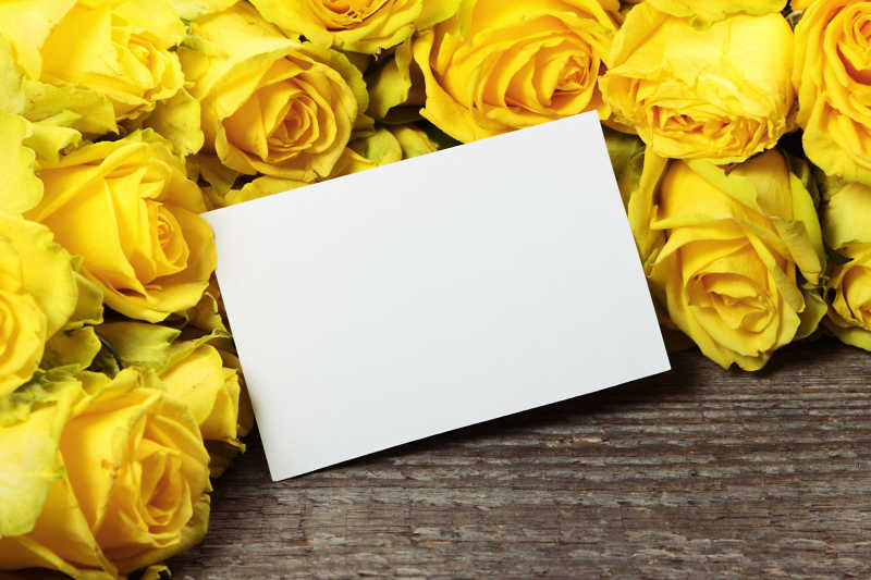 木质桌面上的黄玫瑰花和卡片