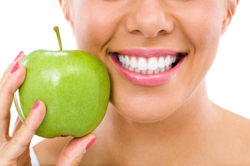 白色背景下女人展示健康的牙齿和绿色苹果