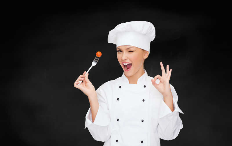 微笑的女厨师一边拿着叉子一边做OK手势